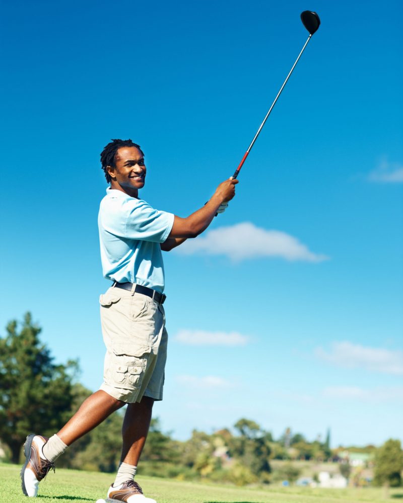 Happy African American golfer practicing his strokes on course