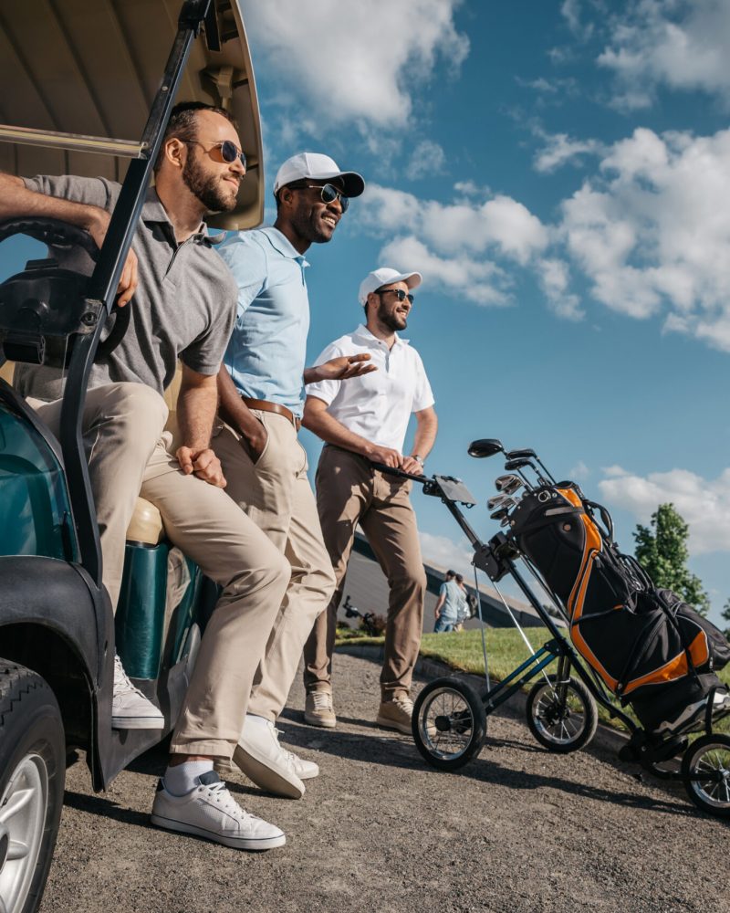 group of smiling friends standing near golf cart and looking away
